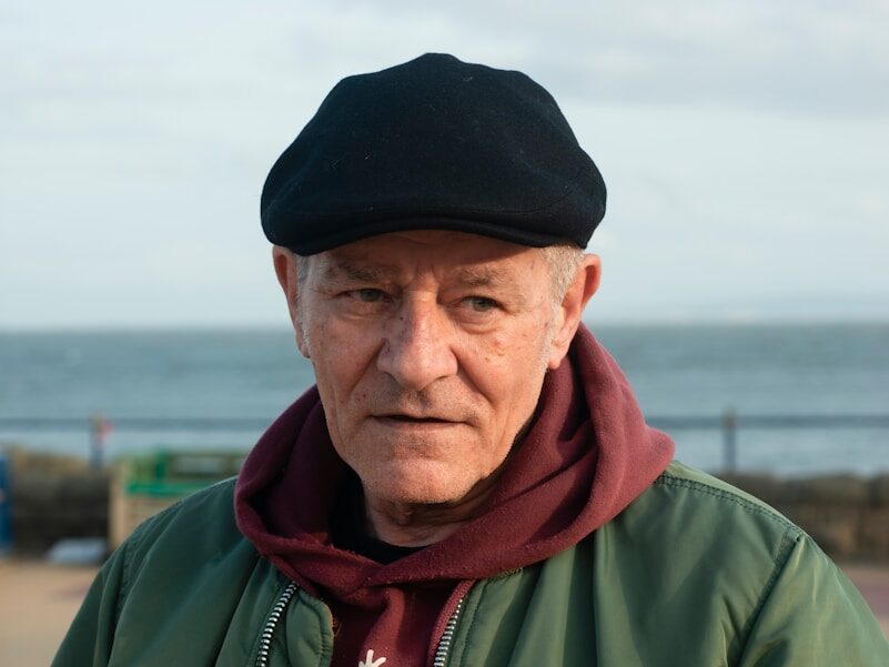 an old man wearing a black hat and a green jacket