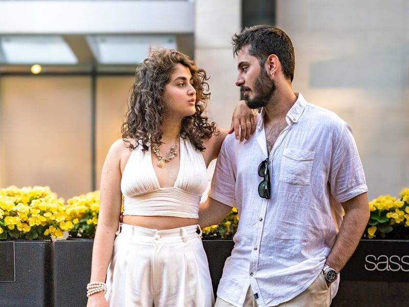 A couple poses together outdoors, looking at each other.