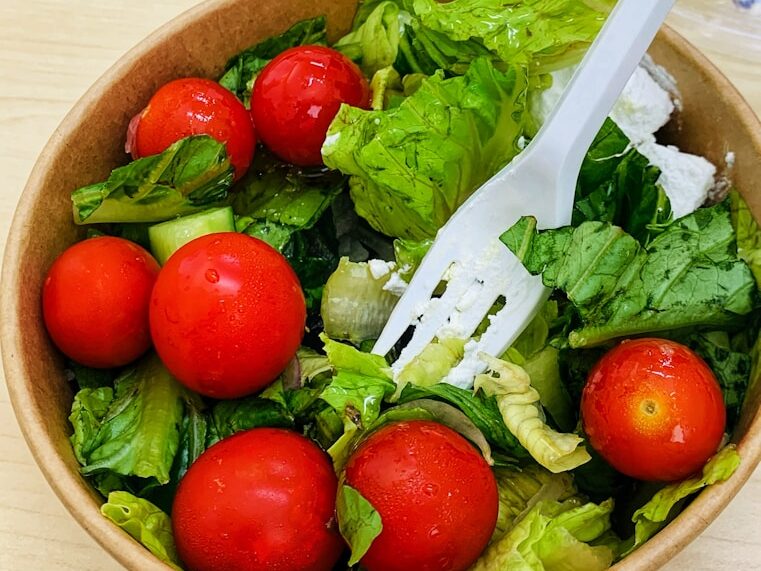A wooden table with a bowl of salad and a plastic fork