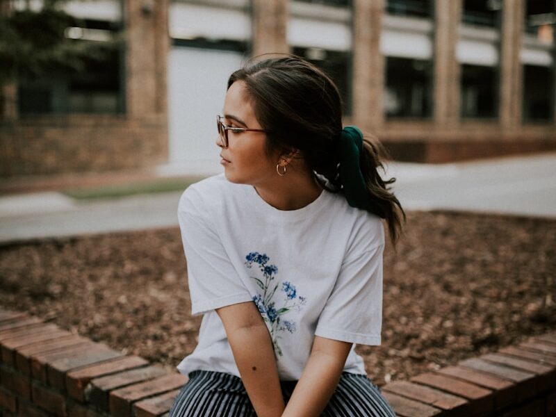 shallow focus photo of woman in white crew-neck T-shirt sitting on concrete bench