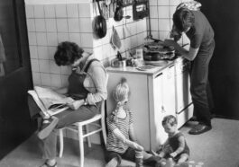 a black and white photo of a woman and two children in a kitchen