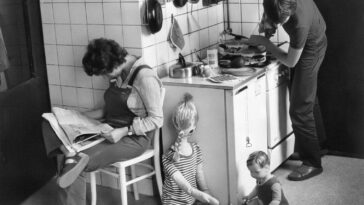 a black and white photo of a woman and two children in a kitchen