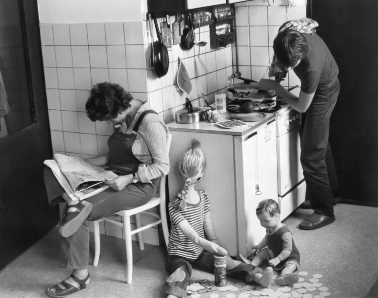 a black and white photo of a woman and two children in a kitchen
