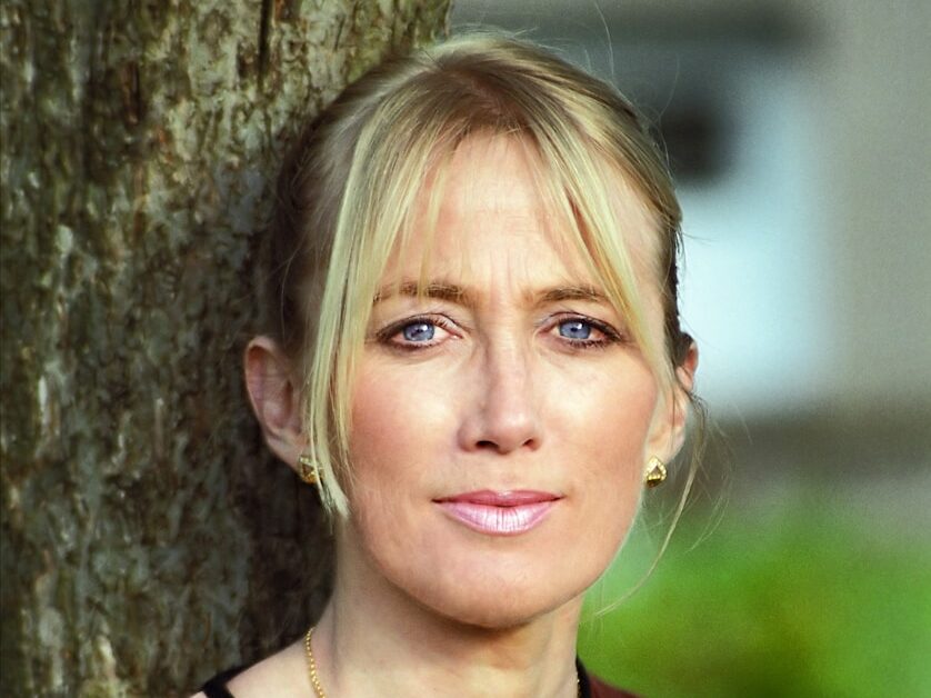 Blonde woman with blue eyes leaning against tree