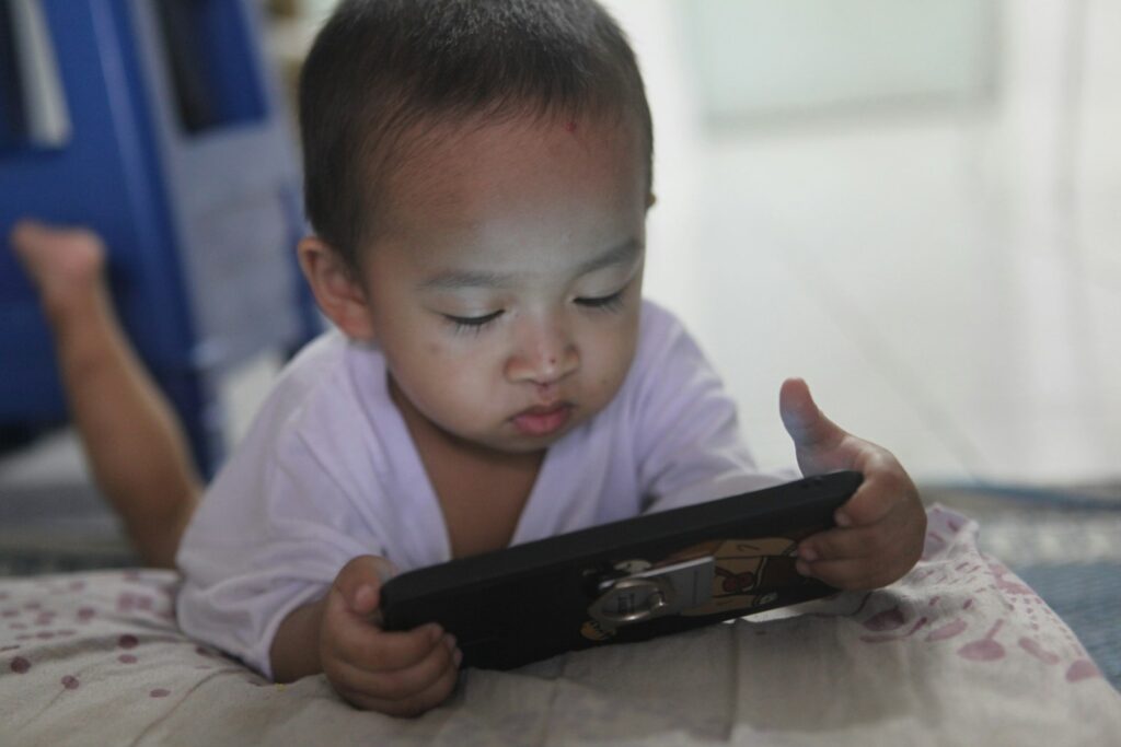 a small child laying on a bed playing with a tablet