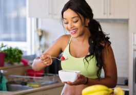 Smiling woman eating a nutritious fruit bowl in a bright kitchen setting.