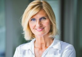 Close-up of a smiling blonde woman wearing eyeglasses indoors.