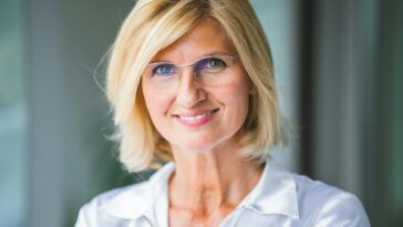 Close-up of a smiling blonde woman wearing eyeglasses indoors.
