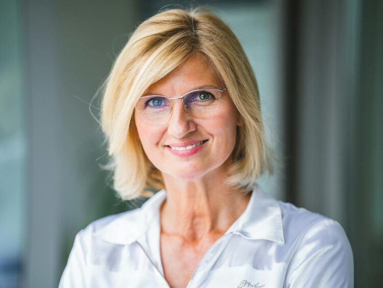 Close-up of a smiling blonde woman wearing eyeglasses indoors.