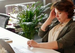 A businesswoman feeling stressed at her home office desk while working on her laptop.