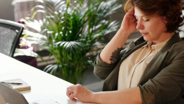 A businesswoman feeling stressed at her home office desk while working on her laptop.