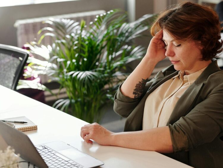 A businesswoman feeling stressed at her home office desk while working on her laptop.