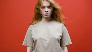 Studio portrait of a woman with long hair wearing a beige t-shirt against a red background.