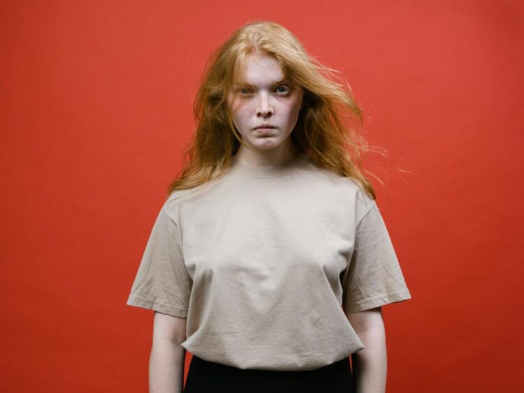 Studio portrait of a woman with long hair wearing a beige t-shirt against a red background.