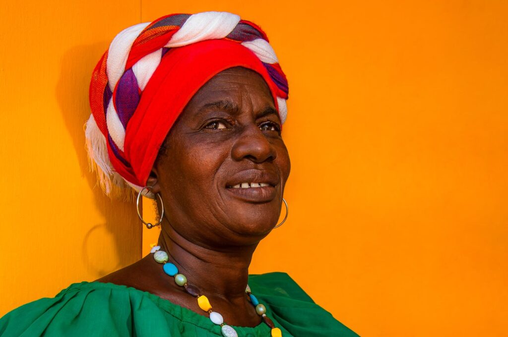 Vibrant portrait of an elderly woman with a colorful turban against an orange backdrop in Cartagena, Colombia.