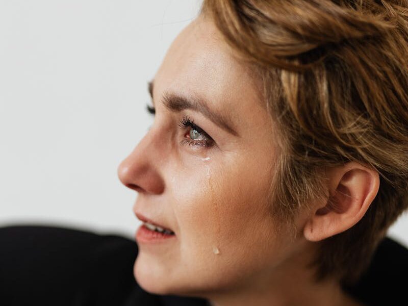 Side view of a woman with teary eyes, holding a guitar, expressing deep emotion and sadness.