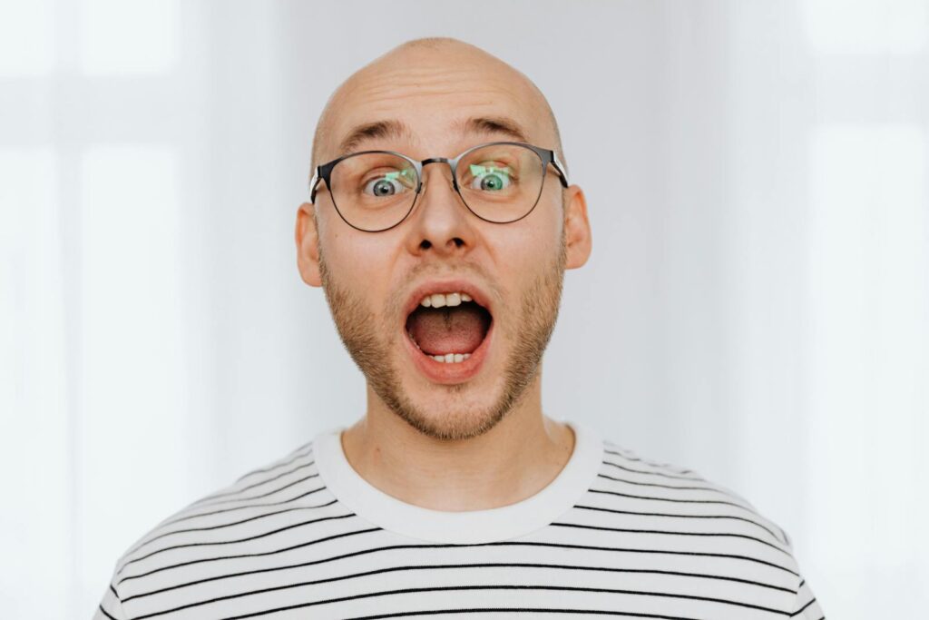 Bald man with glasses expressing surprise in studio setting.